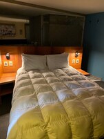 A bed with a quilted headboard, a wooden bedside table, and a wall-mounted light fixture.