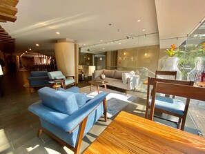 A modern living room with blue sofas, a wooden dining table, and a glass staircase leading to an outdoor area. - Hotel Cle Reforma Insurgentes (Mexico City)
