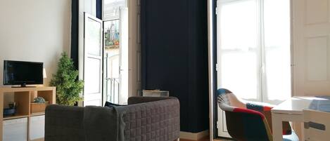A modern room with a bed, a desk, a chair, a television, and a potted plant.