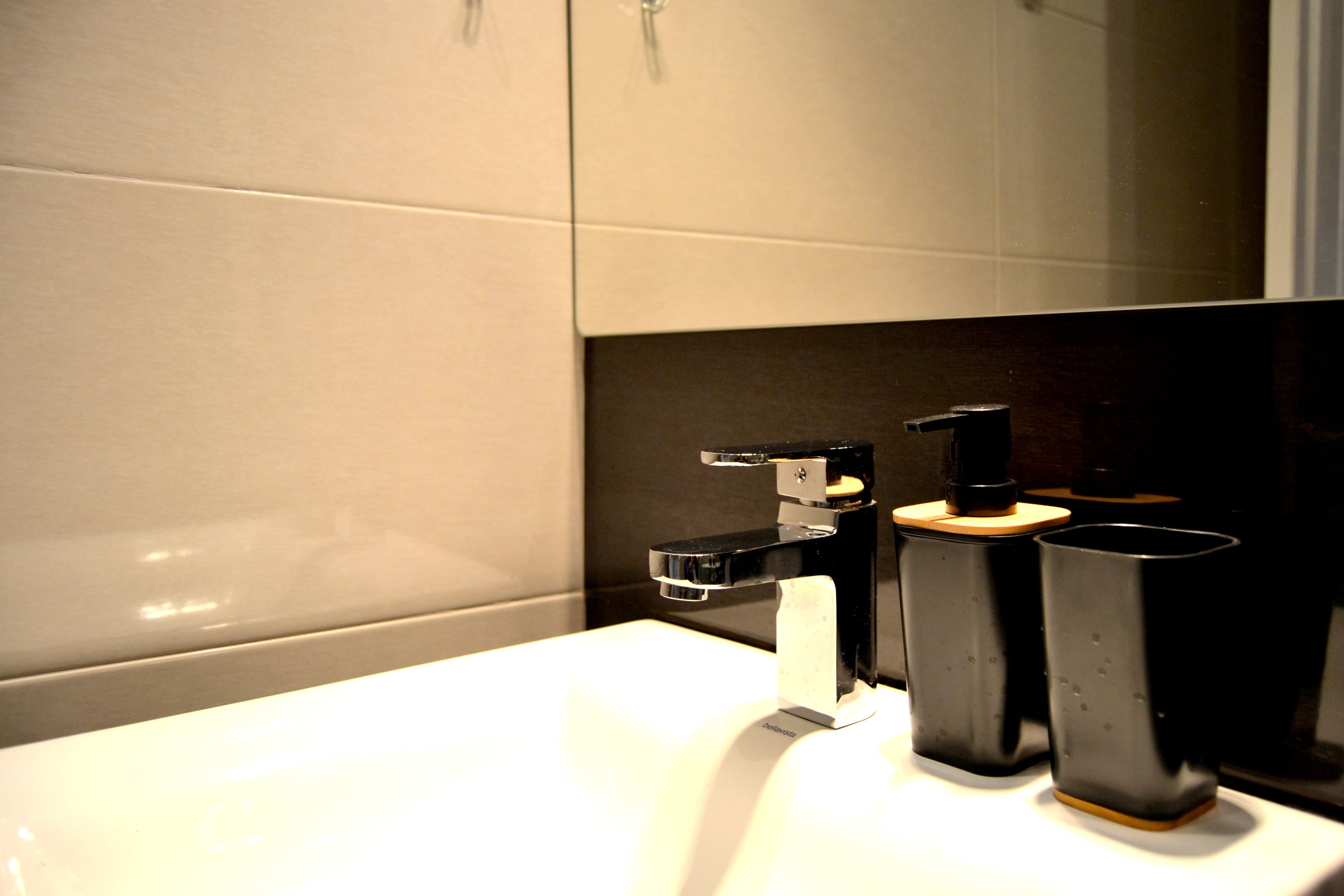 A bathroom with a white sink, black faucet, and two black cups on the counter.