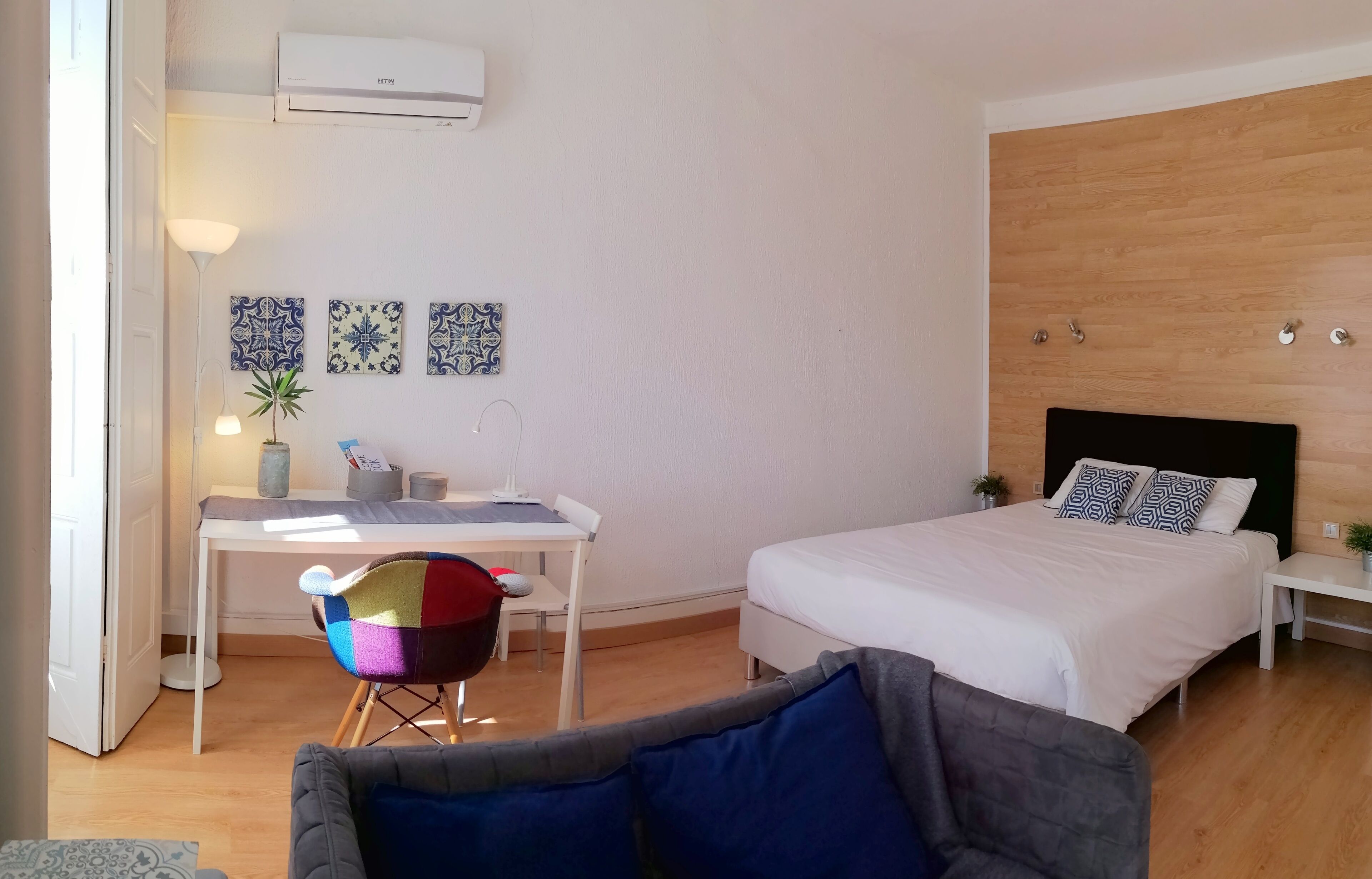 A bedroom with a bed, a desk, a chair, and a bedside table.