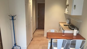 Une cuisine compacte avec une table en bois et des chaises blanches, un lampadaire bleu et une machine à café.