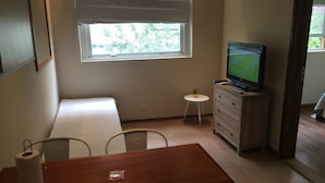 Une petite pièce avec un lit, une table, une télévision et une fenêtre.