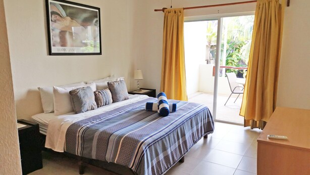 A hotel room with a bed, a nightstand, a lamp, a picture on the wall, and a view of the outside through a sliding glass door. - Las Olas 206 by PRP (Playa del Carmen)