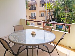 A round glass table with chairs on a balcony, overlooking a building with balconies and palm trees. - Las Olas 206 by PRP (Playa del Carmen)