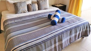 A neatly made bed with a striped bedspread and rolled towels, a nightstand with a lamp, and a framed picture on the wall. - Las Olas 206 by PRP (Playa del Carmen)