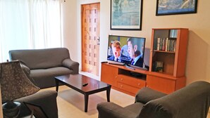 A living room with a sofa, a coffee table, a TV on a wooden stand, and a bookshelf. - Las Olas 206 by PRP (Playa del Carmen)