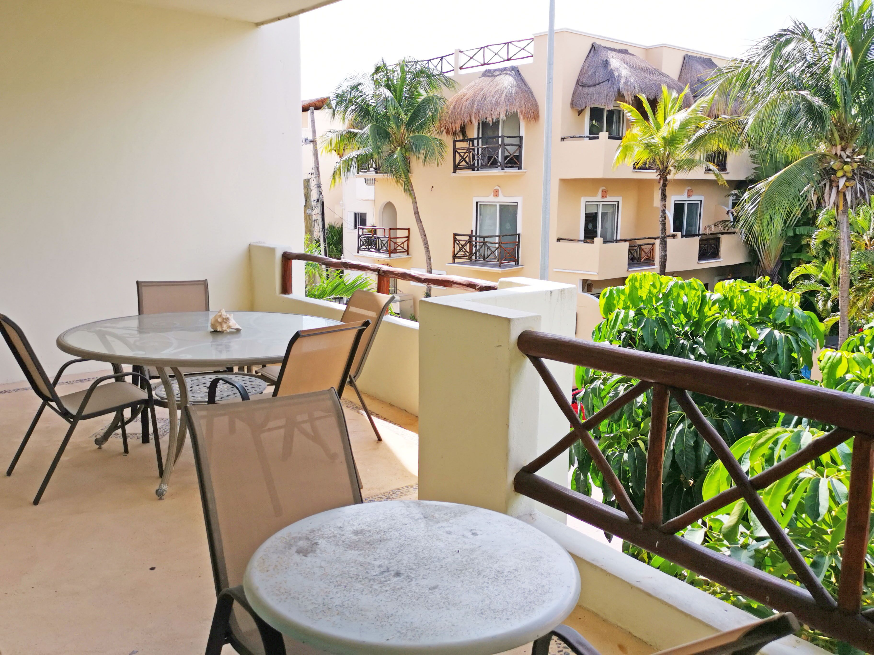 A balcony with a round table and chairs, overlooking a building with balconies and palm trees.