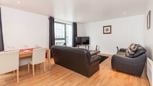 Un salon moderne avec un canapé, une table à manger dressée pour deux personnes et un téléviseur.