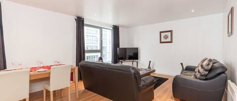 A modern living room with a sofa, a dining table set for two, and a television.