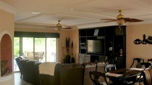 A living room with a sectional sofa, a television, and a dining area with chairs and a table. - Casa Lin (Mazatlán)