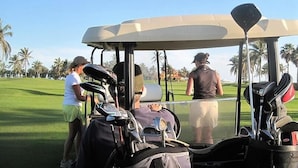 A golf cart with a driver and caddy, a golf bag, and a person in a white shirt and green shorts. - Casa Lin (Mazatlán)