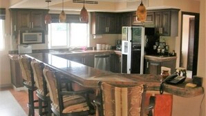 A kitchen with a central island, bar stools, hanging pendant lights, and dark cabinetry. - Casa Lin (Mazatlán)