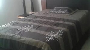 A neatly made bed with a dark-colored bedspread and decorative pillows, a bedside table with a lamp, and a mirror on the wall. - Casa Lupita (Mazatlán)