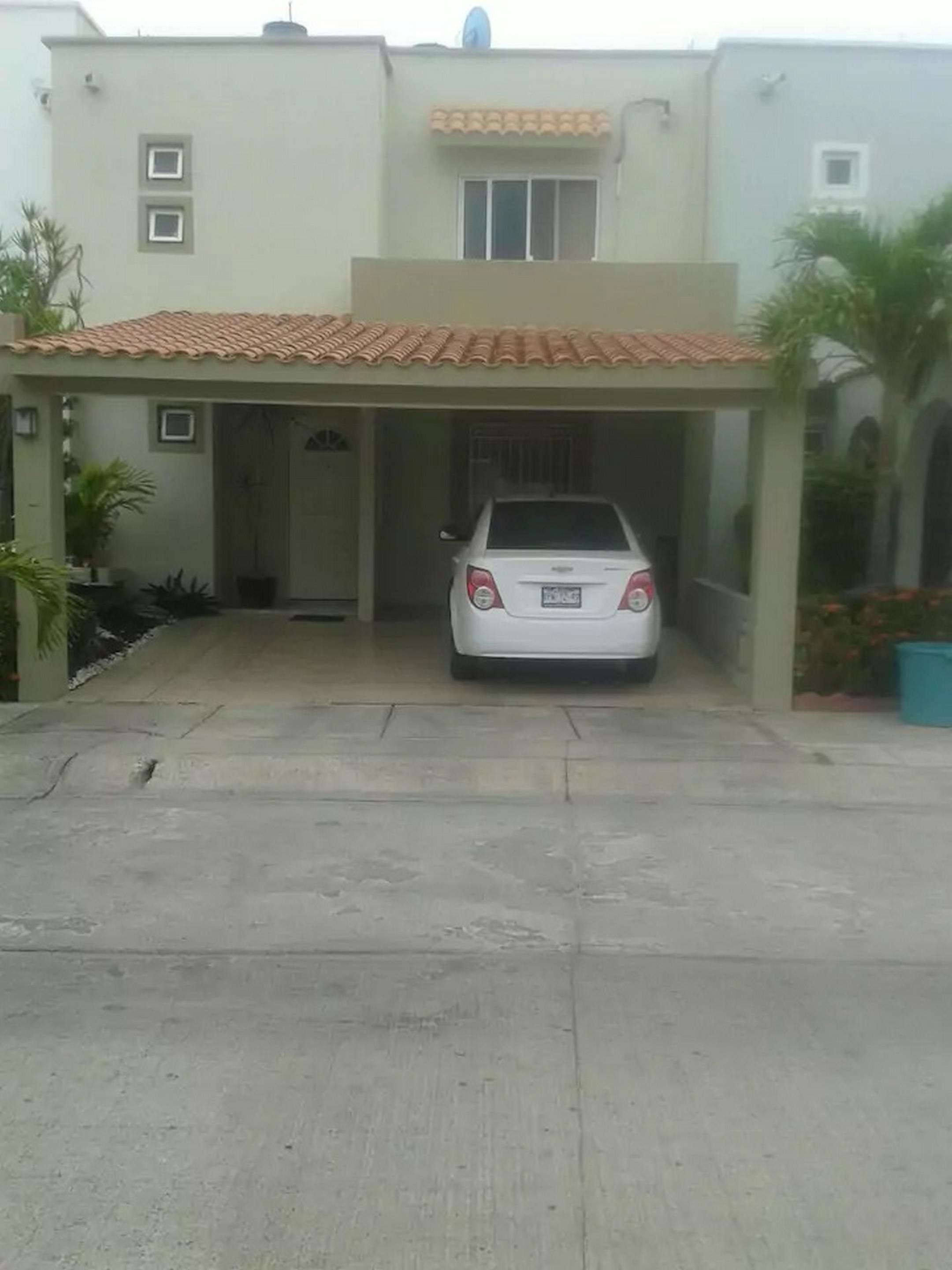 Un edificio de dos pisos con un coche estacionado bajo un garaje cubierto.