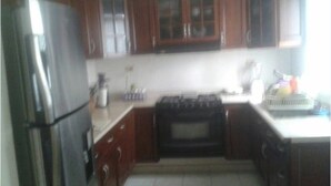 A kitchen with wooden cabinets, a stainless steel refrigerator, a stove, and a sink. - Casa Lupita (Mazatlán)