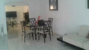 A living room with a white sofa, a dining table with chairs, a TV on a stand, and a ceiling fan. - Casa Lupita (Mazatlán)