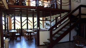 Un vaste espace dédié à la salle à manger, avec des tables et des chaises en bois, un escalier et une vue sur l’extérieur.