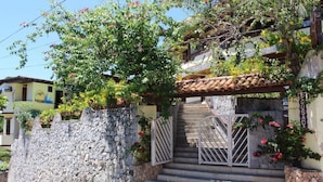 Un mur de pierre, un escalier et une porte menant à un bâtiment dont le toit est recouvert de tuiles.