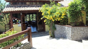 Un bâtiment avec un toit recouvert de tuiles et une porte d’entrée en bois. On aperçoit un mur de pierre et une clôture en bois au premier plan.
