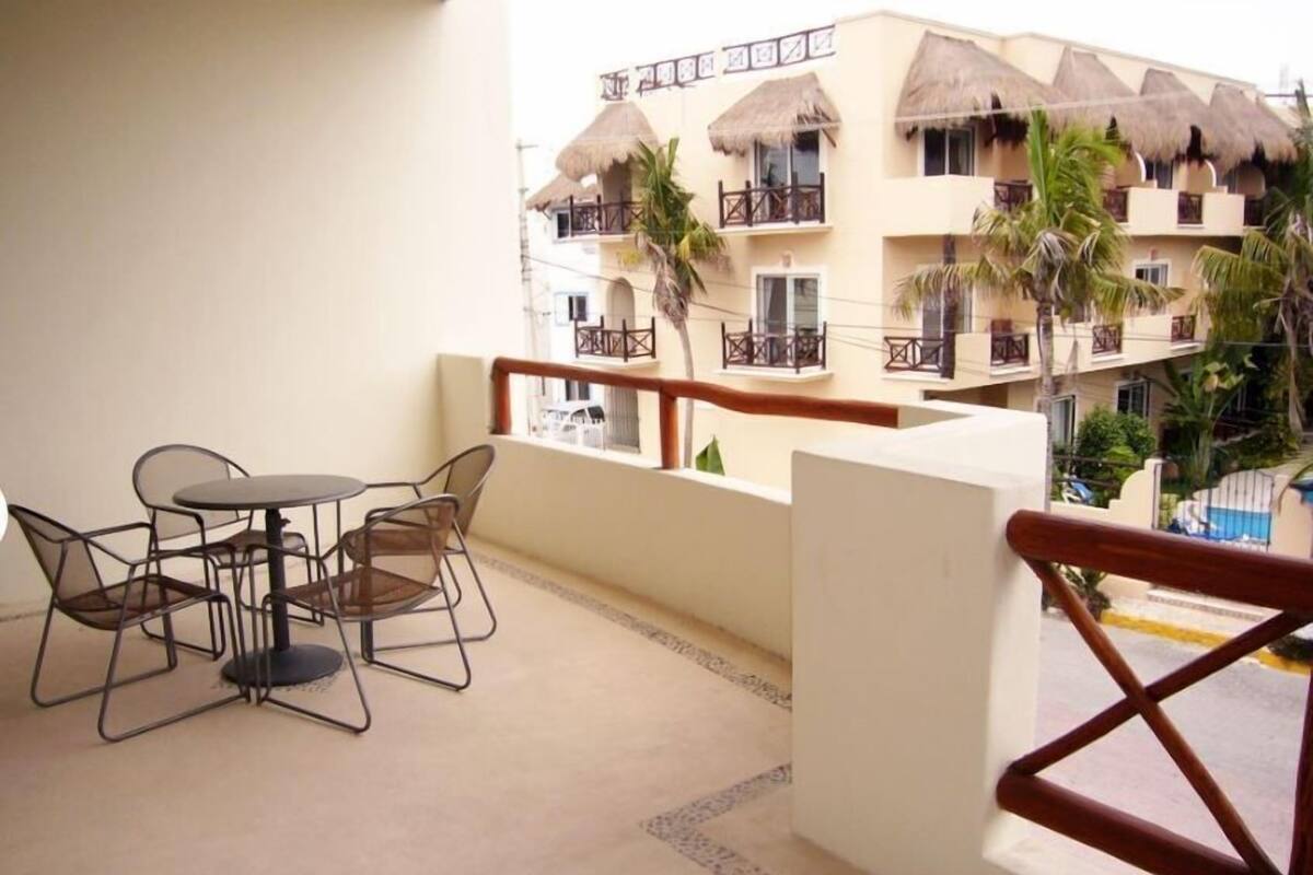 Ein Balkon mit Tisch und Stühlen, Blick auf ein Gebäude mit mehreren Balkonen und Palmen.