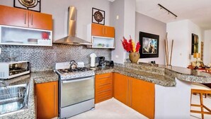 A modern kitchen with granite countertops, stainless steel appliances, and orange cabinetry. - Las Olas family Townhome Apartments (Playa del Carmen)