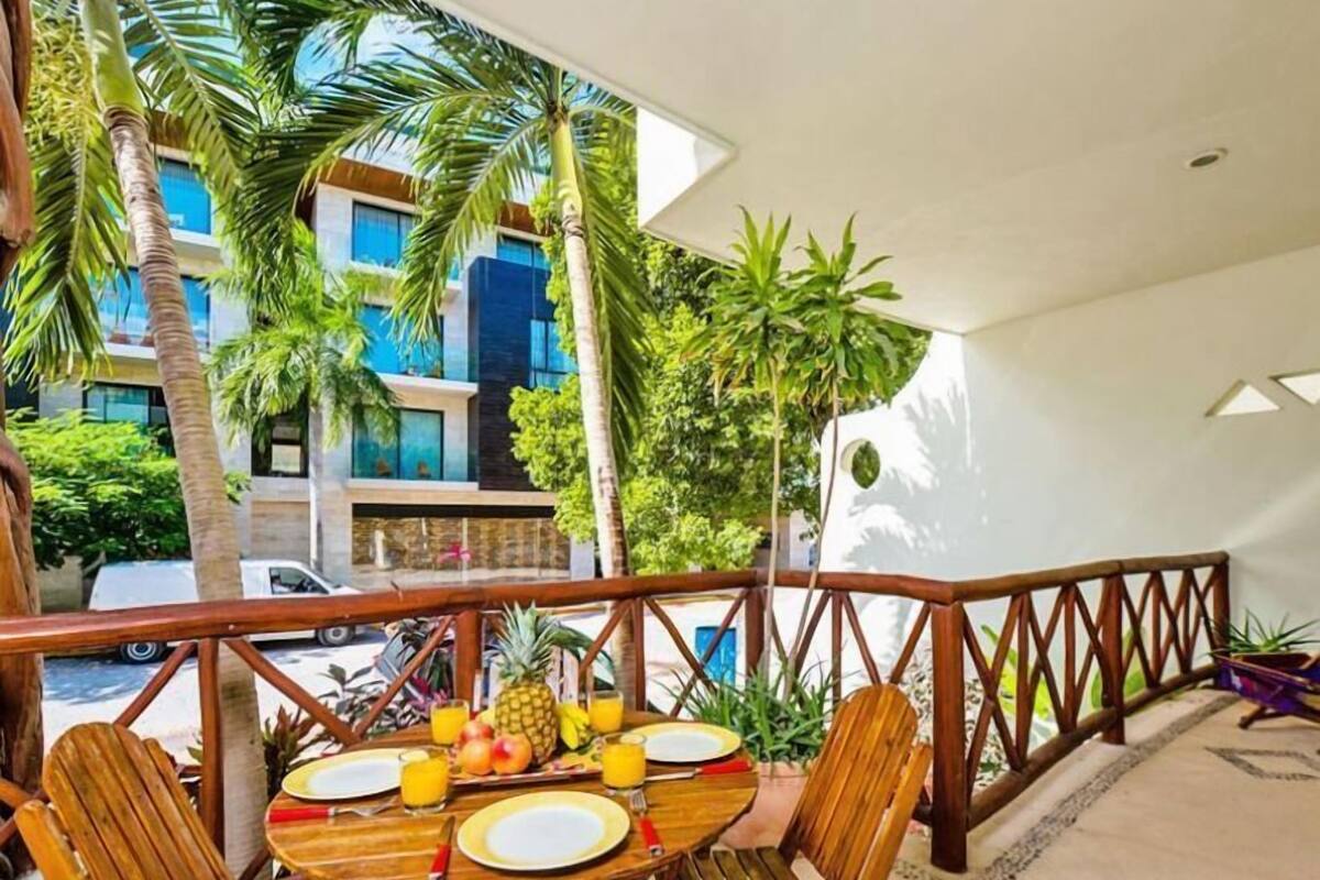 Ein Holztisch mit Tellern, Besteck und Obst auf einem Balkon mit Blick auf einen Pool und Palmen.