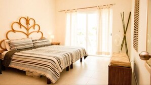 A bedroom with a bed, a nightstand, a bedside table, a window with curtains, and a wall-mounted plant. - Las Olas family Townhome Apartments (Playa del Carmen)