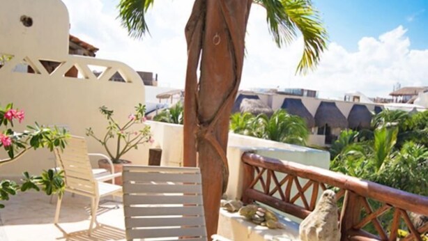A terrace with two white lounge chairs, a wooden table, and a palm tree. - Las Olas family Townhome Apartments (Playa del Carmen)