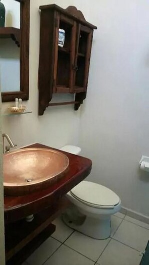 A bathroom with a wooden cabinet, a copper sink, and a white toilet.