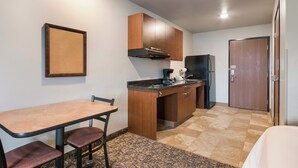 A compact kitchen with a dining table and chairs, a refrigerator, and wooden cabinets.
