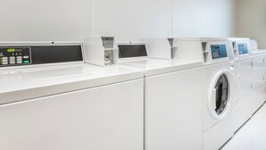 A row of white, modern, front-loading washing machines in a clean, white-walled laundry room.