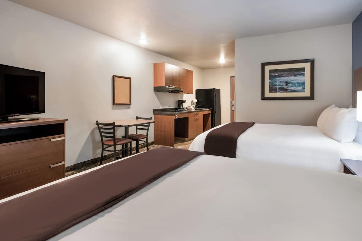 A hotel room with two beds, a desk, a television, and a kitchenette.