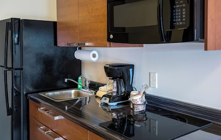 A kitchen with a black refrigerator, a microwave, a coffee maker, and wooden cabinets.. My Place Hotel - Davenport/Quad Cities IA