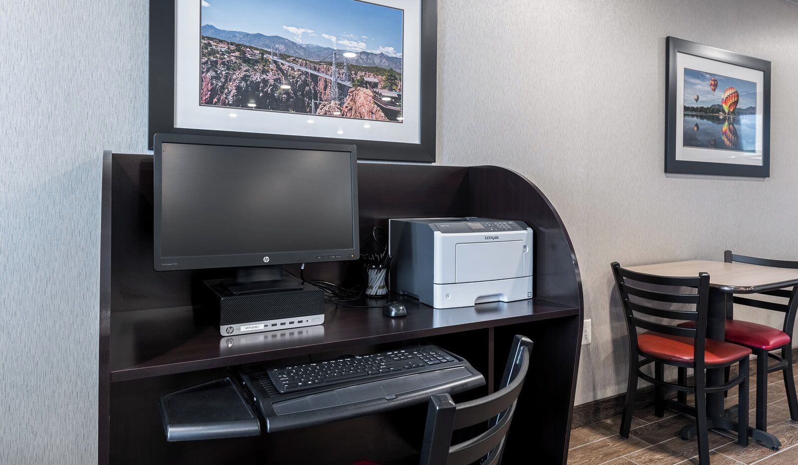 Un espace de travail dans un hôtel, équipé d’un ordinateur de bureau, d’une imprimante et d’une chaise.