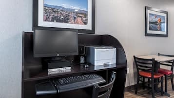 Un espace de travail dans un hôtel, équipé d’un ordinateur de bureau, d’une imprimante et d’une chaise.