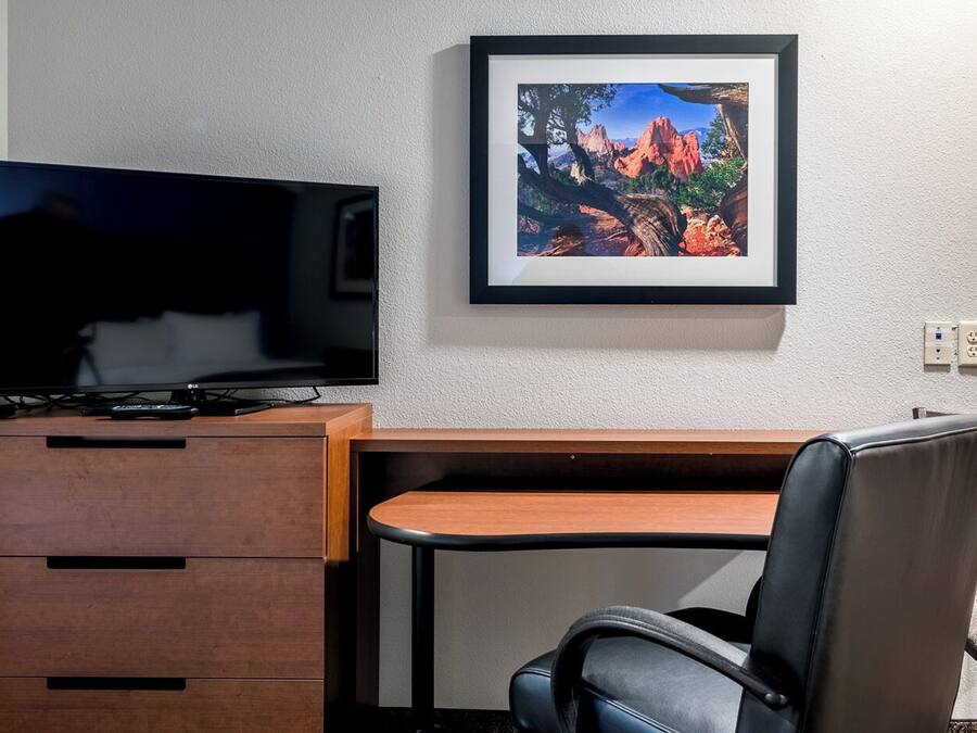 A modern room with a wooden desk, a black leather chair, a flat-screen TV, and a framed picture on the wall.