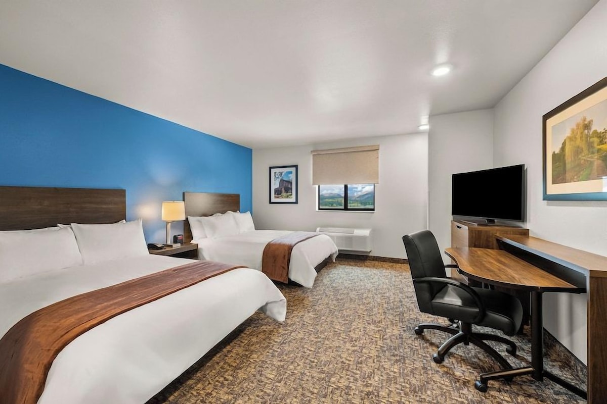 A hotel room with two beds, a desk, a TV, a window, and a painting on the wall.