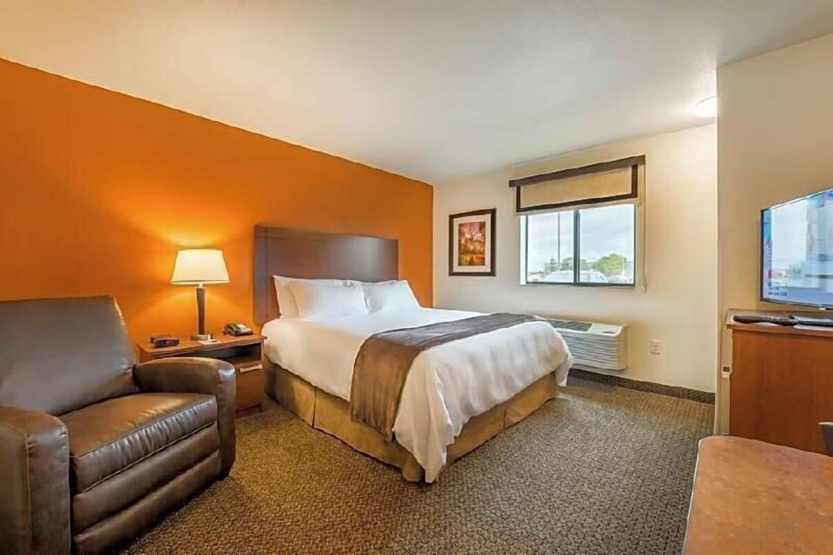 A hotel room with a bed, a chair, a desk, a lamp, a television, and a window.