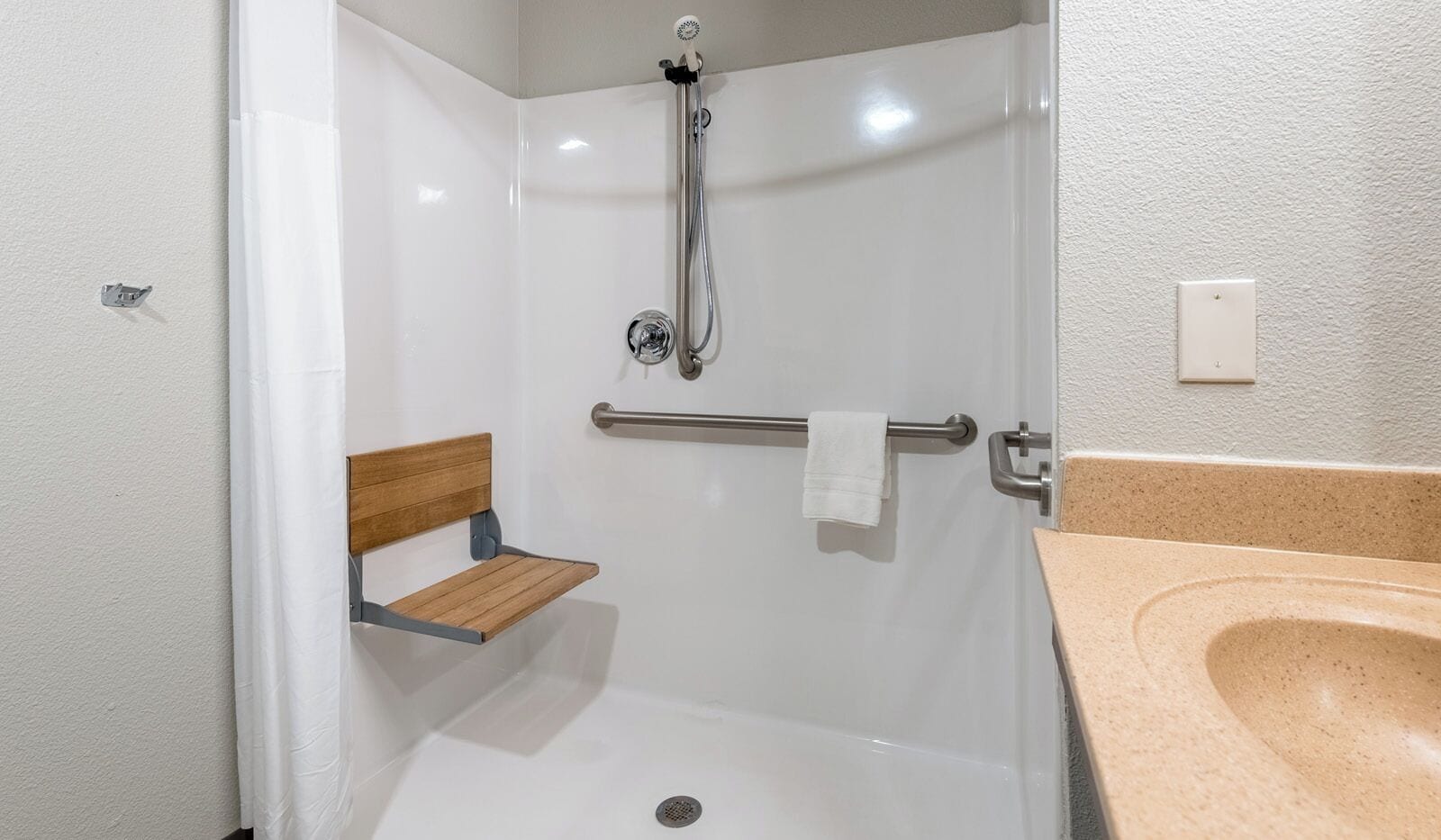 A shower with a bench, a towel rack, and a sink with a beige countertop.