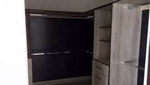 Un vestidor con pared trasera oscura, panel frontal de madera clara y barra metálica.