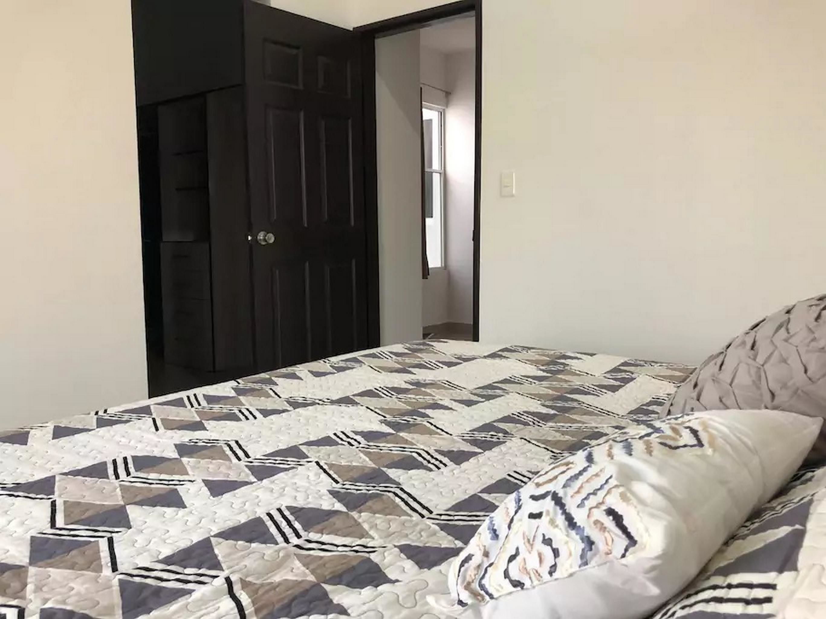 Un dormitorio con cama, una colcha estampada y una puerta oscura.