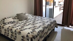 Un dormitorio con cama, ropa de cama estampada y vistas a través de una puerta corrediza de vidrio.
