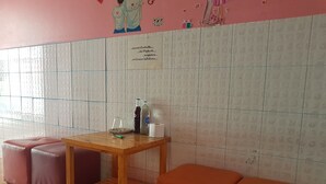 A small seating area with a wooden table and two cushioned stools, a tiled wall with a decorative mural, and a bottle of soda on the table. - Wanjai Resort (Warin Chamrap)