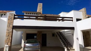 A modern house with a stone facade, a car parked in the driveway, and a staircase leading to the upper level. - Casita Selin C (Mazatlán)