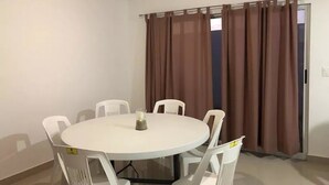 A small, round dining table with six white chairs, a candle, and a window with brown curtains. - Casita Selin C (Mazatlán)