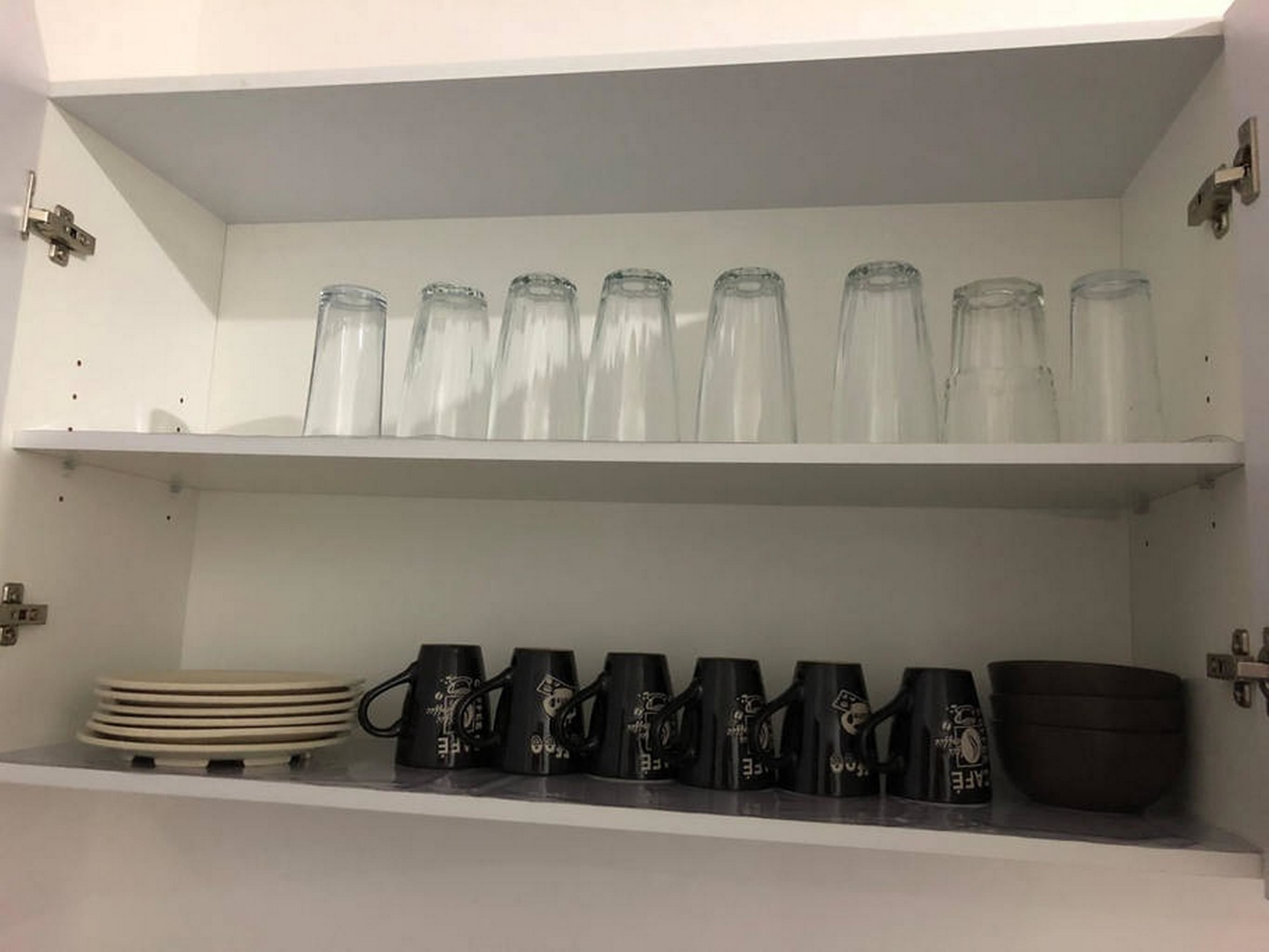A kitchen shelf with glass jars and black mugs.