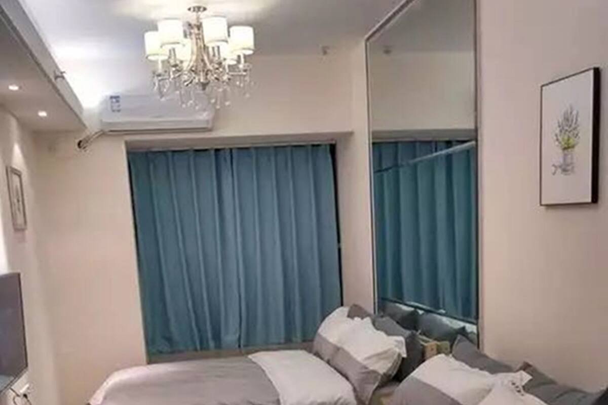 Un dormitorio con cama, espejo, candelabro y ventana con cortinas.