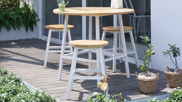 A patio with a wooden table and four white chairs, surrounded by potted plants and a large glass door. - Nan Nakara Boutique (Nan)