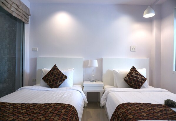 A hotel room with two beds, each with a white headboard, a bedside table with a lamp, and a window with a view. - Nan Nakara Boutique (Nan)